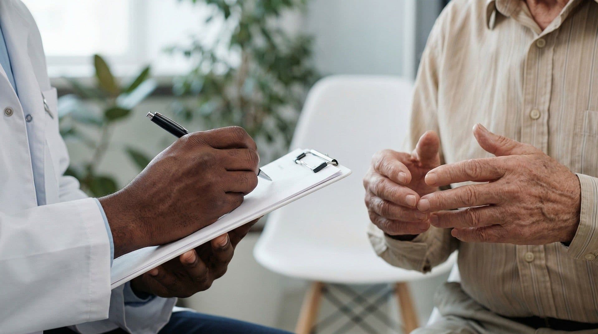 Arzt im Gespräch mit einem älteren Patienten, Notizen auf einem Klemmbrett